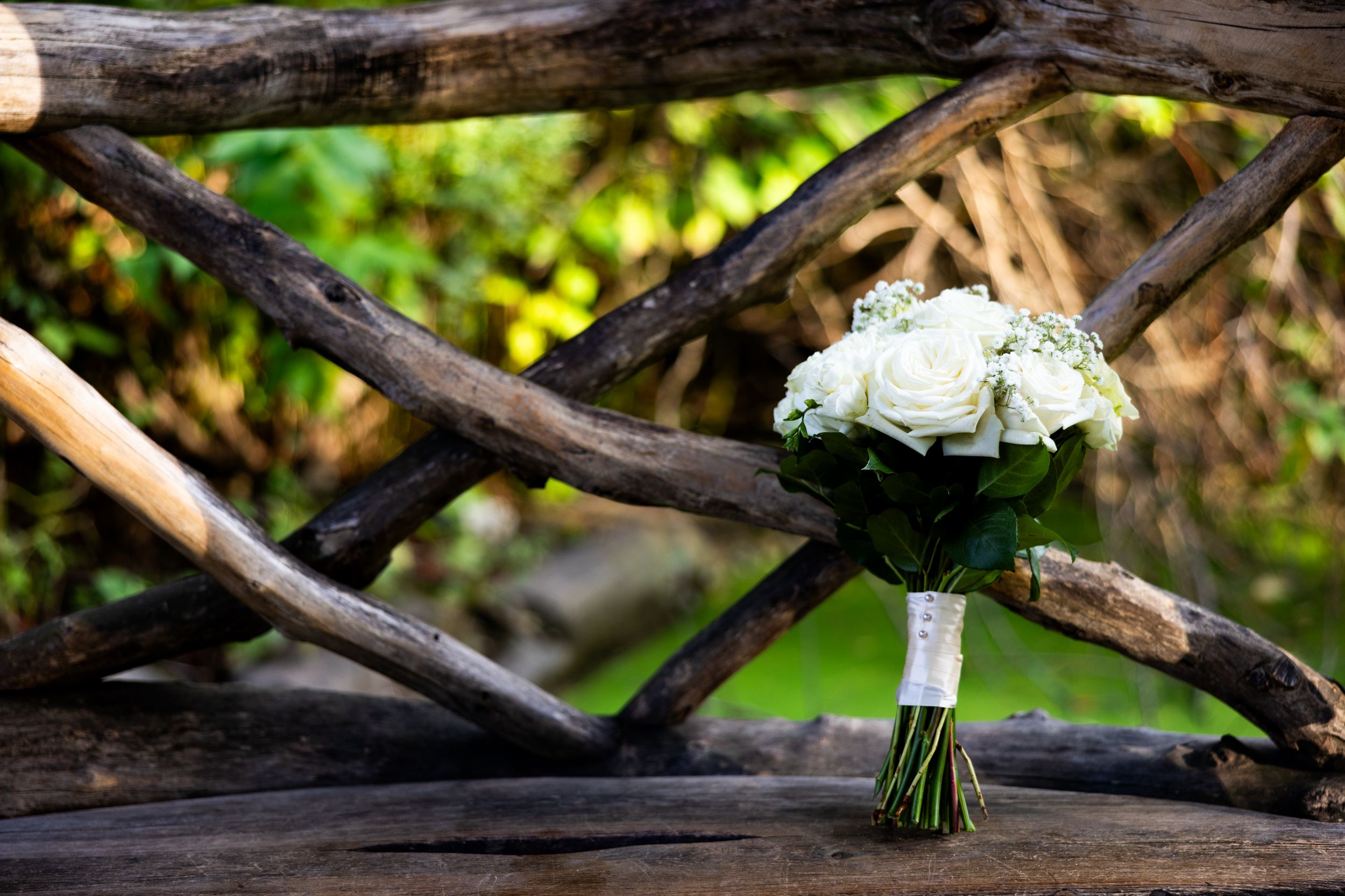 A white rose wedding bouquet rests on weathered wooden rails in natural lighting.