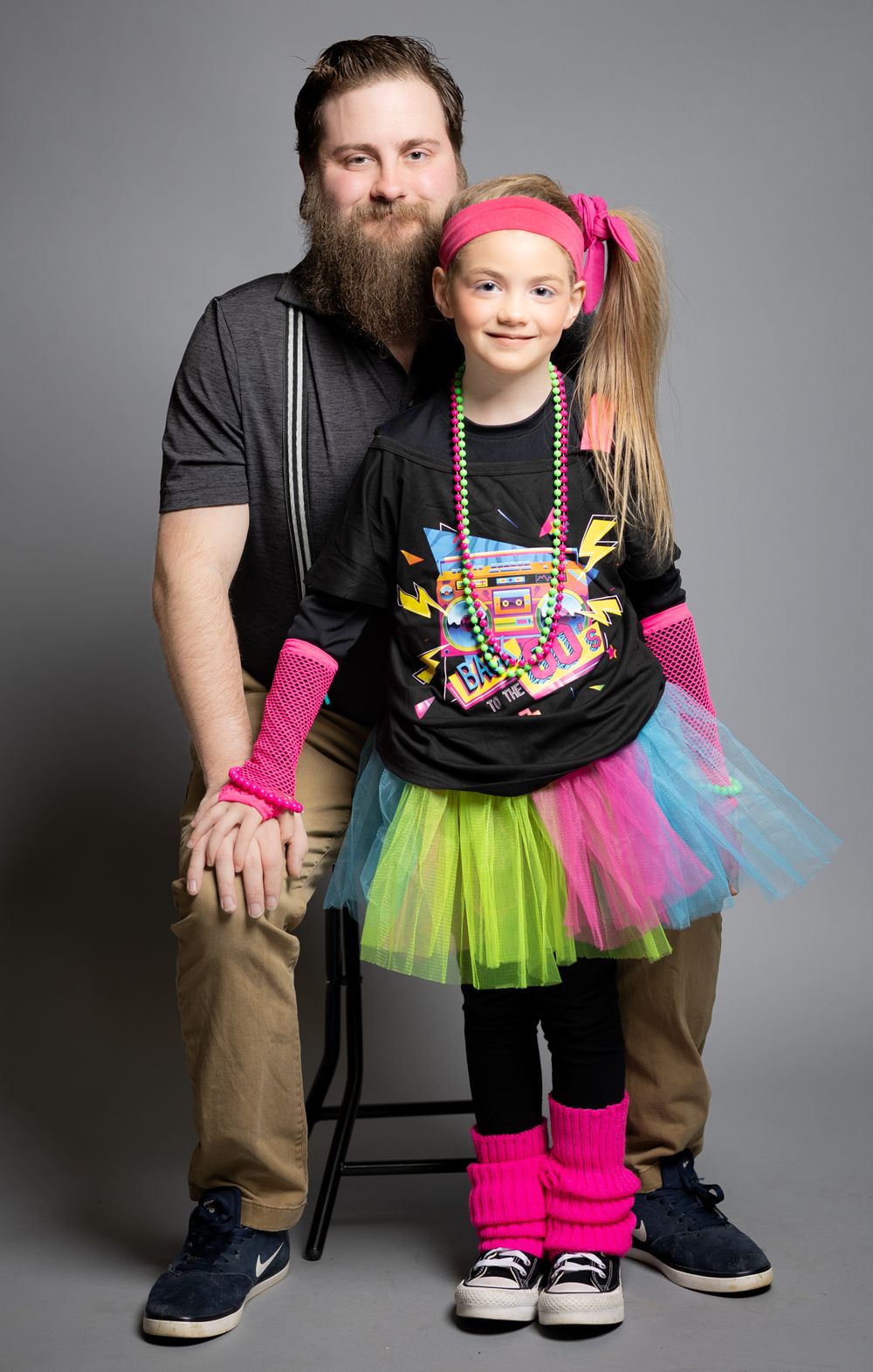 Portrait with adult and child wearing colorful neon accessories and tutu against grey background.