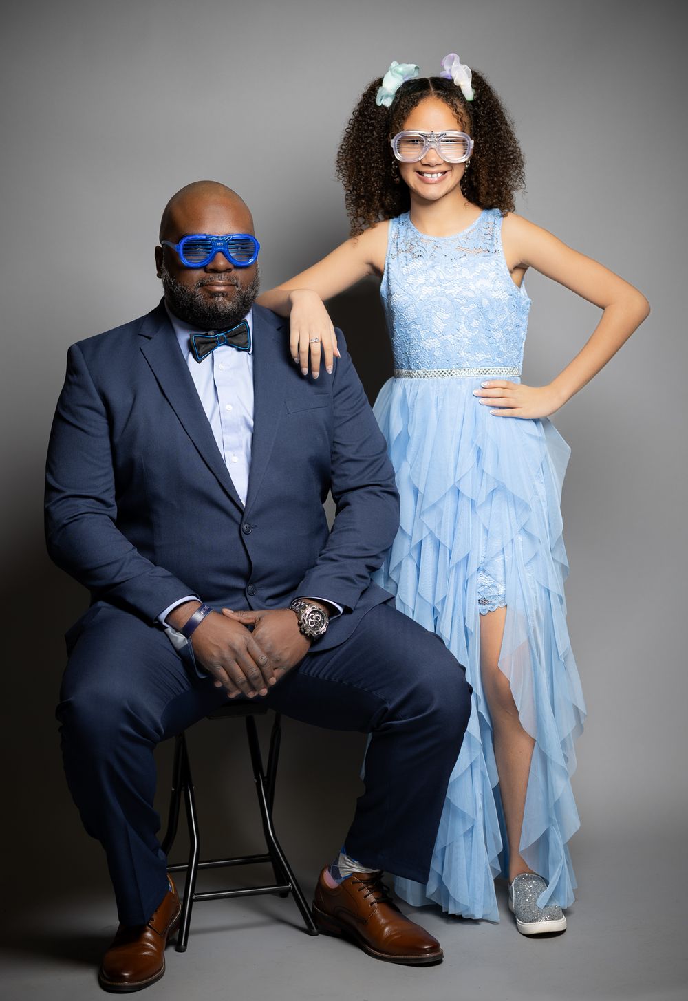 Formal portrait of two people in elegant blue attire against a dark gray studio background.