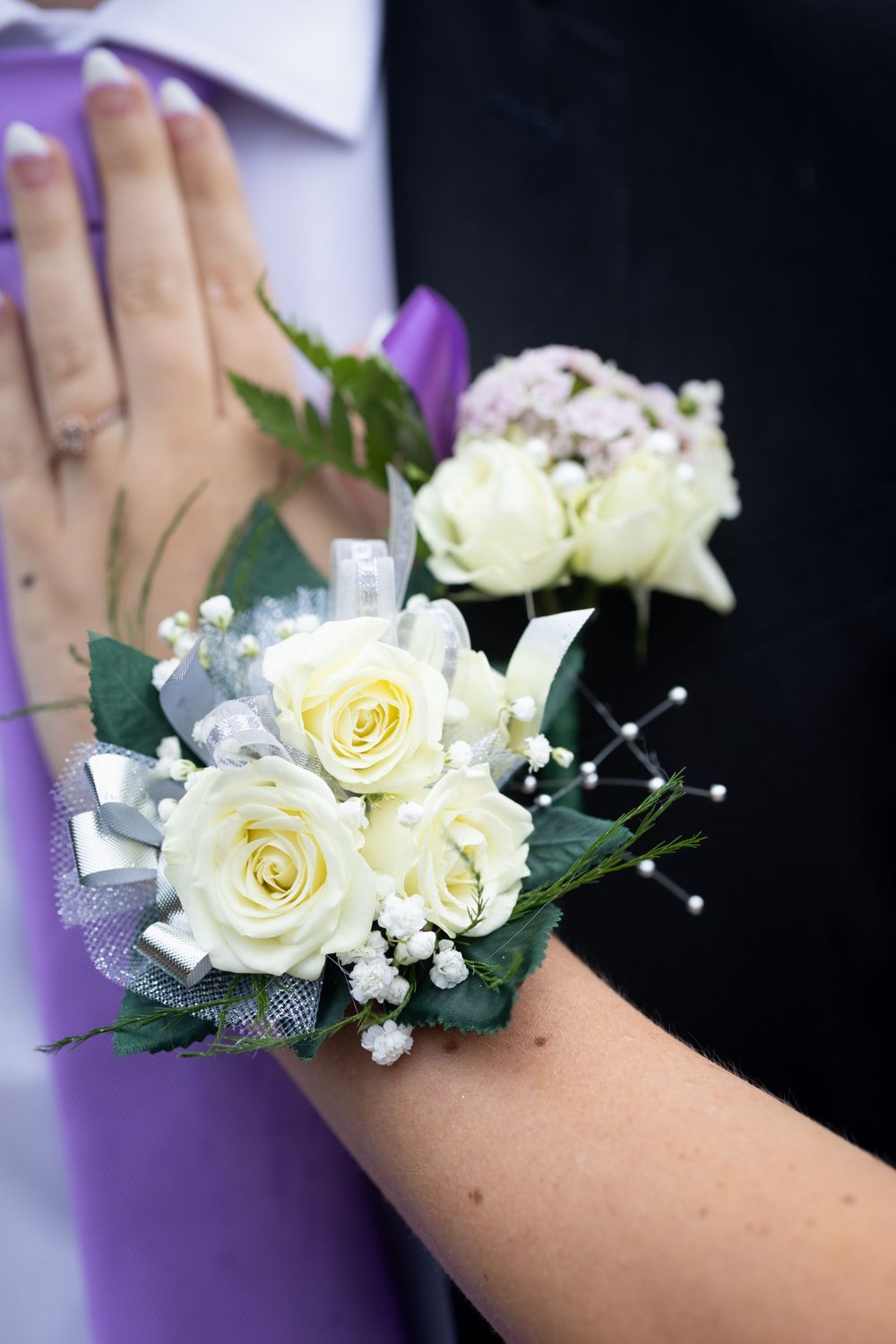 A delicate white rose and purple wristlet corsage with baby's breath and ribbon details.