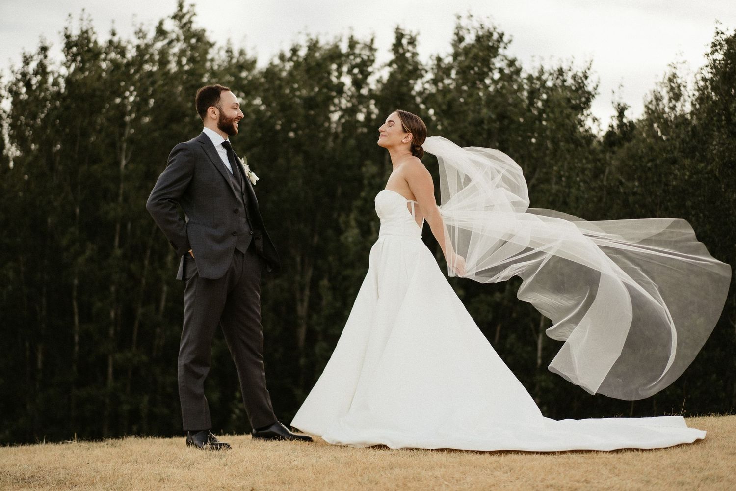 Black and white wedding photo of a couple resting on a grassy hill with dramatic mountain peaks in the background.