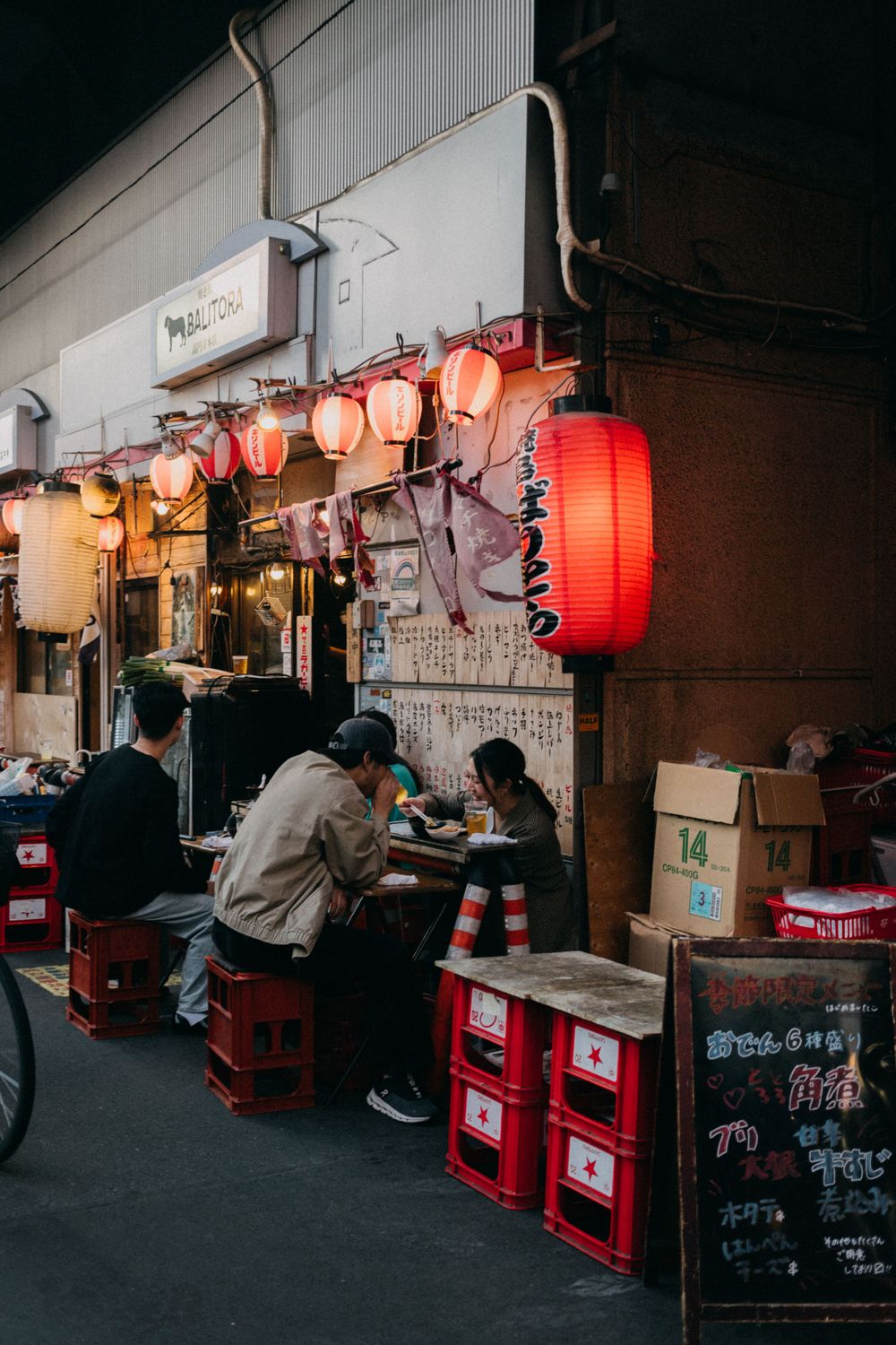 Japanese street food stall with red lanterns and diners at night.