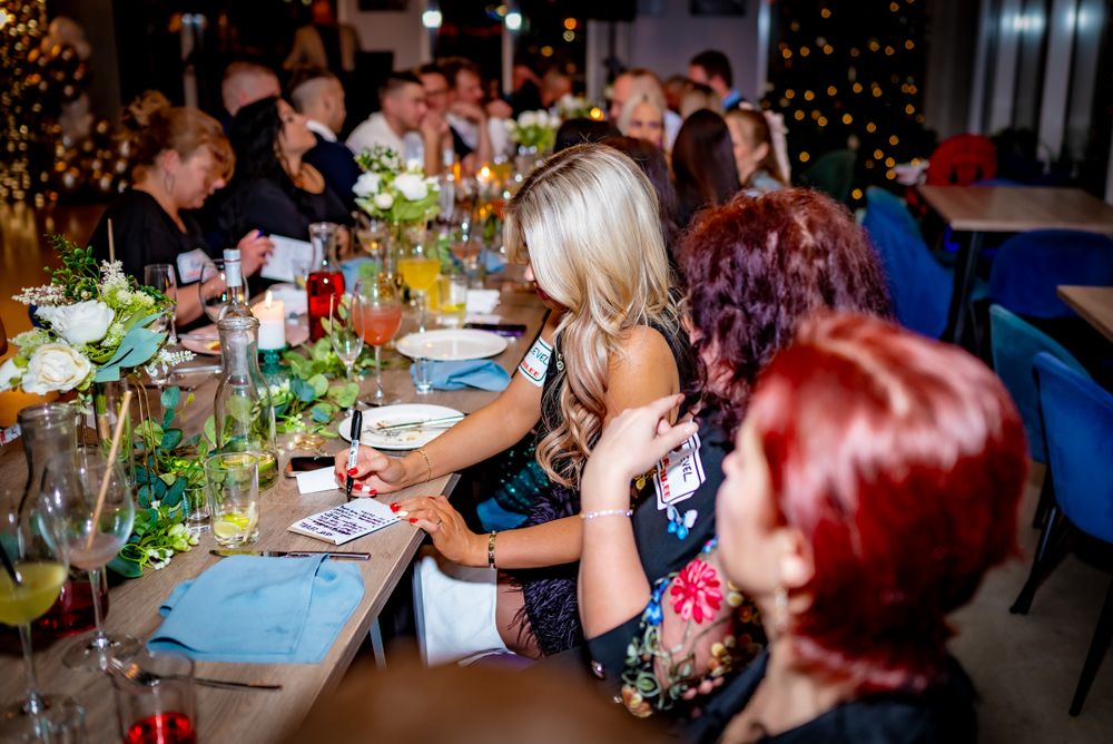 Festive dinner party with guests seated at a decorated table with greenery and ambient lighting.