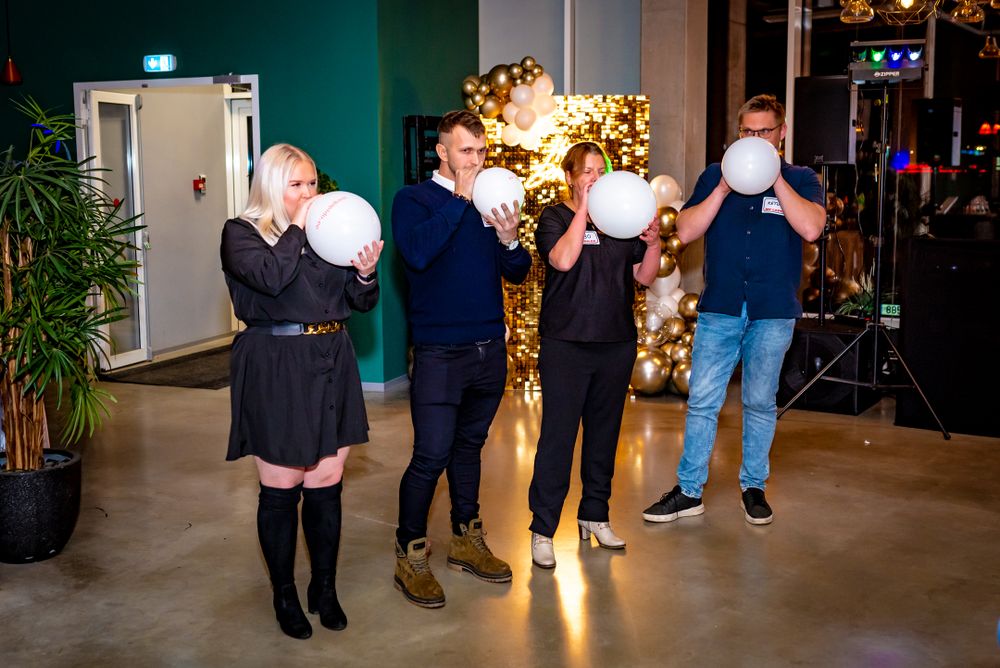 Group activity with people blowing up white balloons in front of a golden balloon wall decoration.