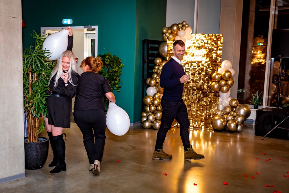 People preparing balloon decorations near a gold balloon wall with indoor plants.