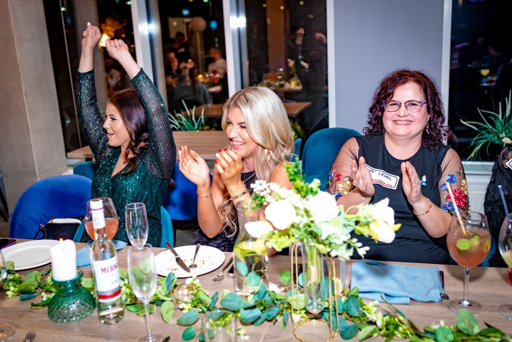 Guests enjoy drinks and conversation at an elegant evening party with floral centerpieces and green decor.