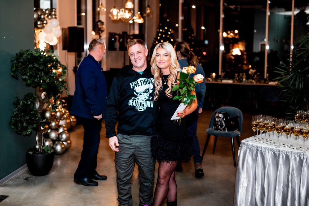 Party guests socializing near a decorated holiday tree and buffet table at an evening celebration.