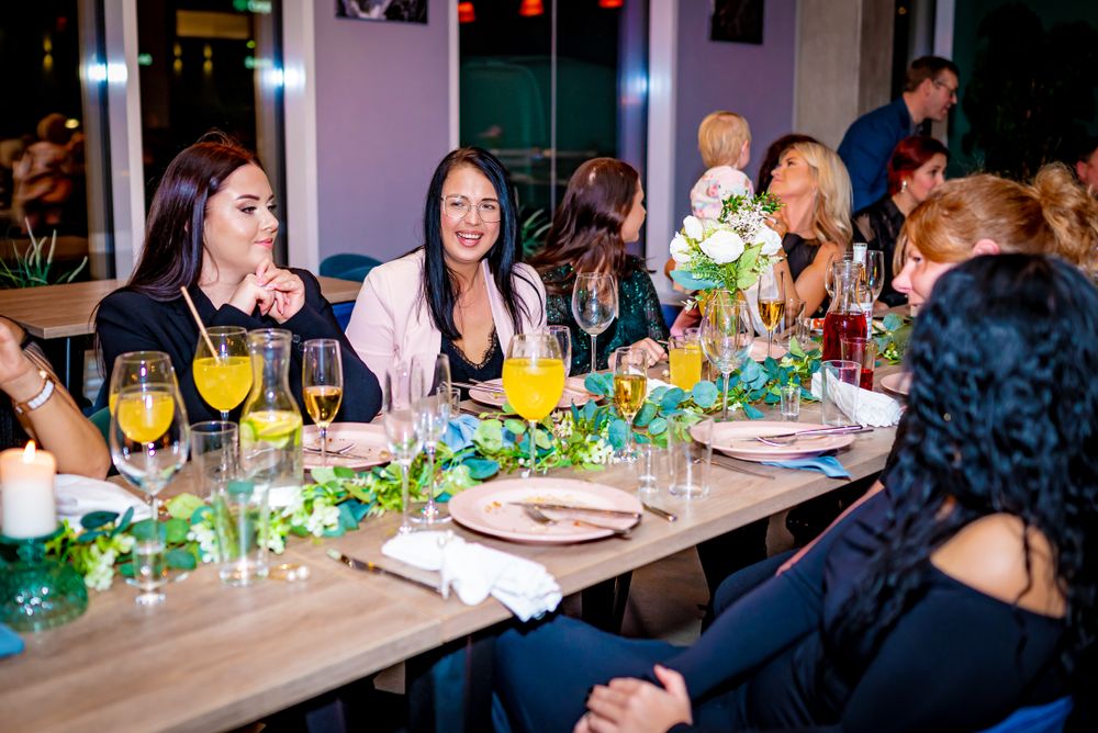 Dinner guests enjoying conversation at decorated table with floral centerpieces and string lights.