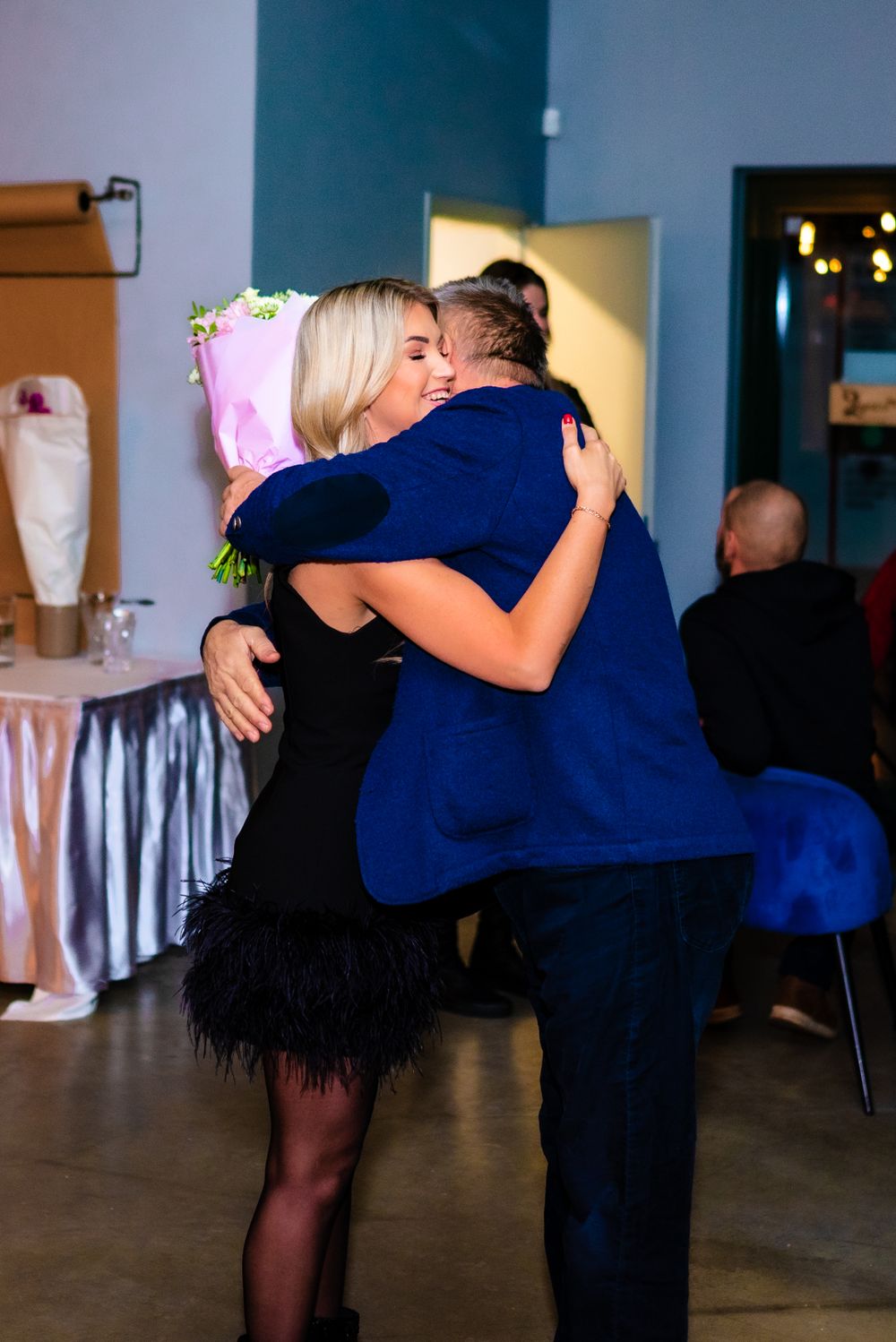 Warm embrace shared between party guests at elegant evening celebration with holiday decor.
