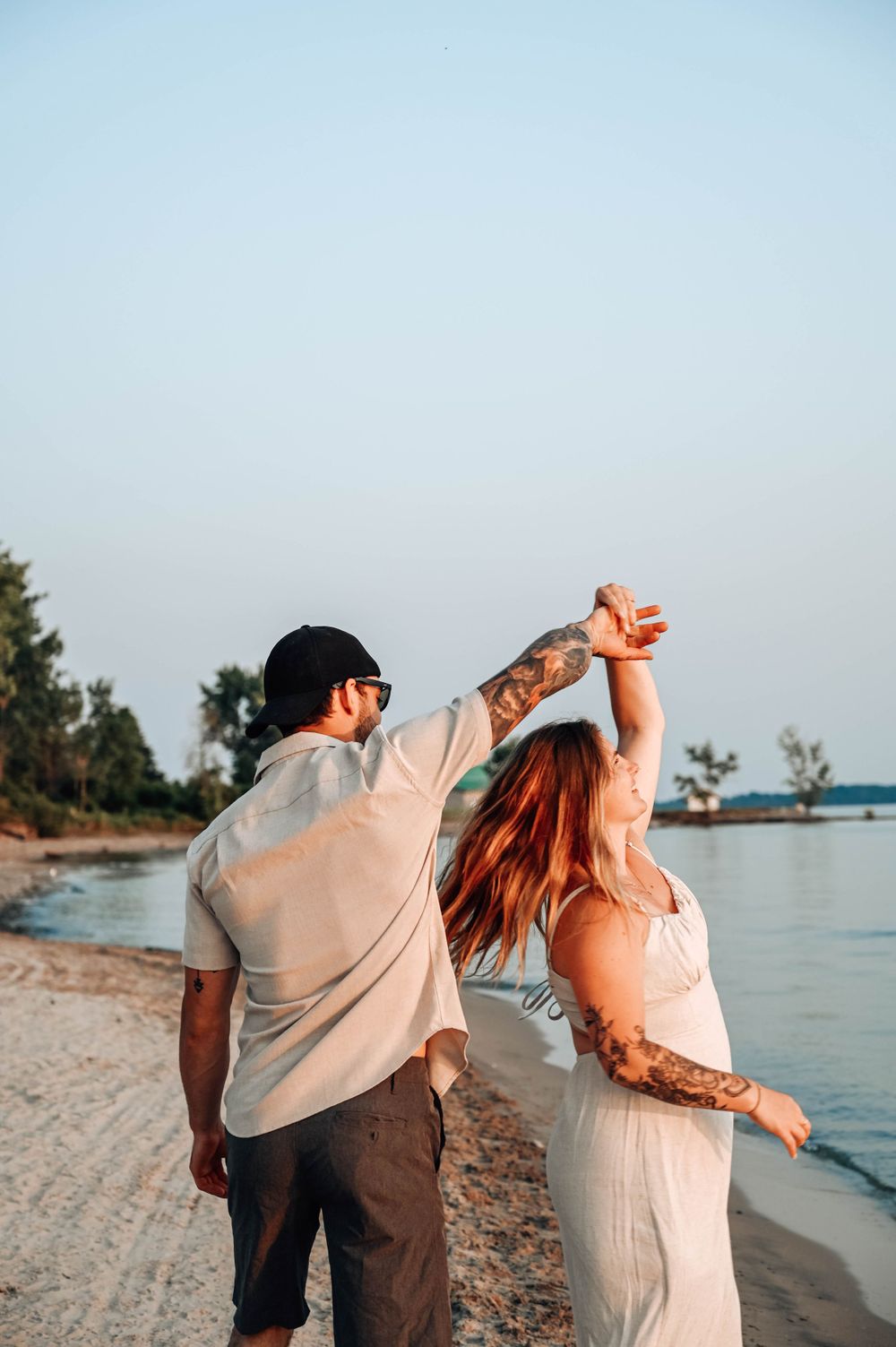 A couple dances together on a beach at sunset with the ocean and trees visible in the background.