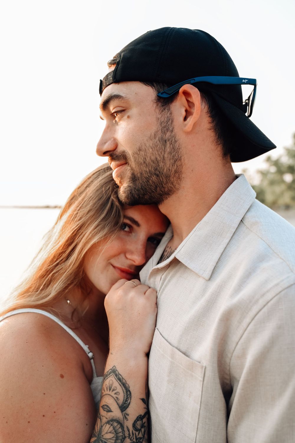 A loving couple shares an intimate moment at sunset, with one wearing a backwards cap while the other rests against them.