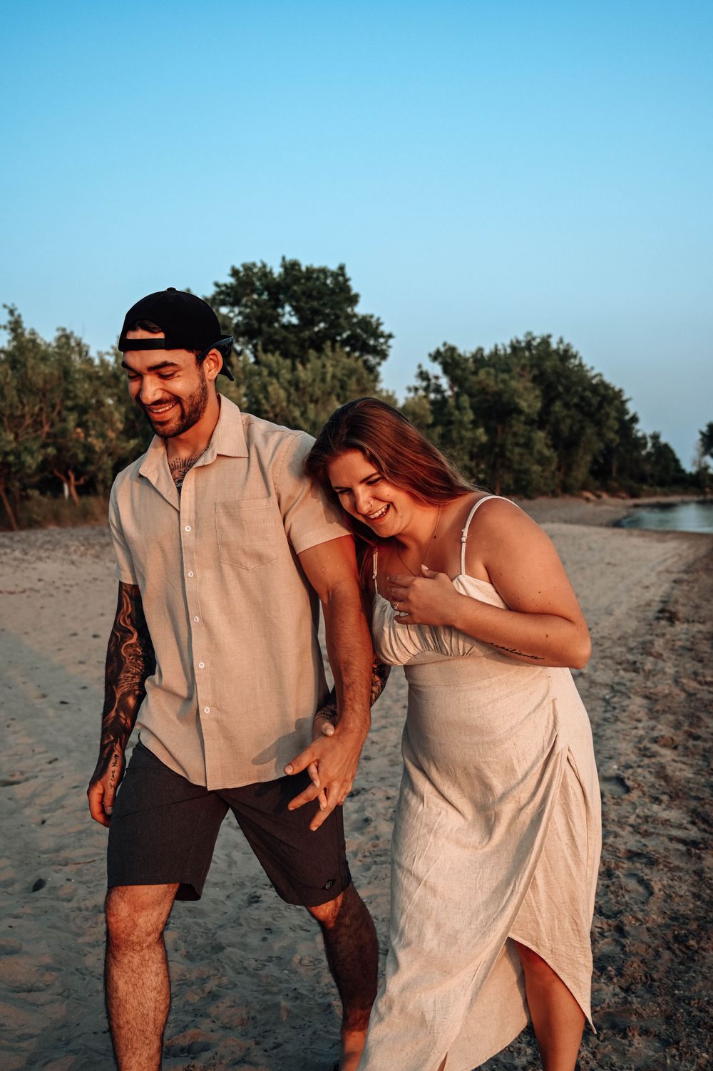 A couple laughs together while walking along a sandy beach at sunset on a clear summer day.