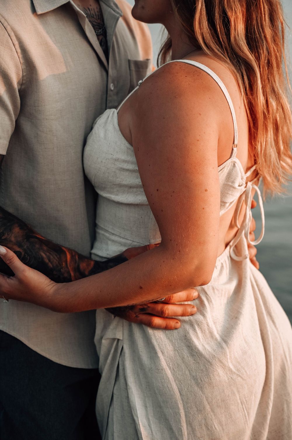 A romantic couple embraces while wearing light colored clothing during an intimate outdoor photoshoot.
