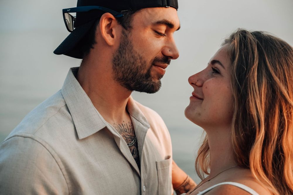 A couple shares an intimate moment smiling at each other in warm lighting during sunset.