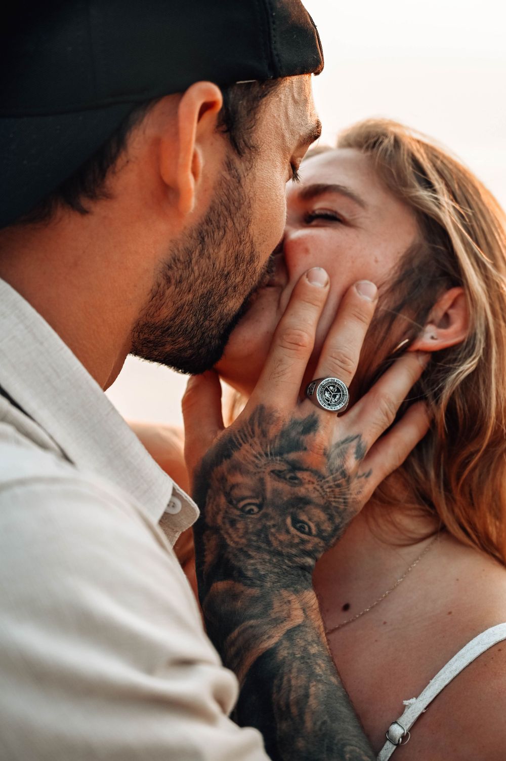 Close up romantic photo of a tender kiss with one partner displaying detailed tattoo artwork on their hand.