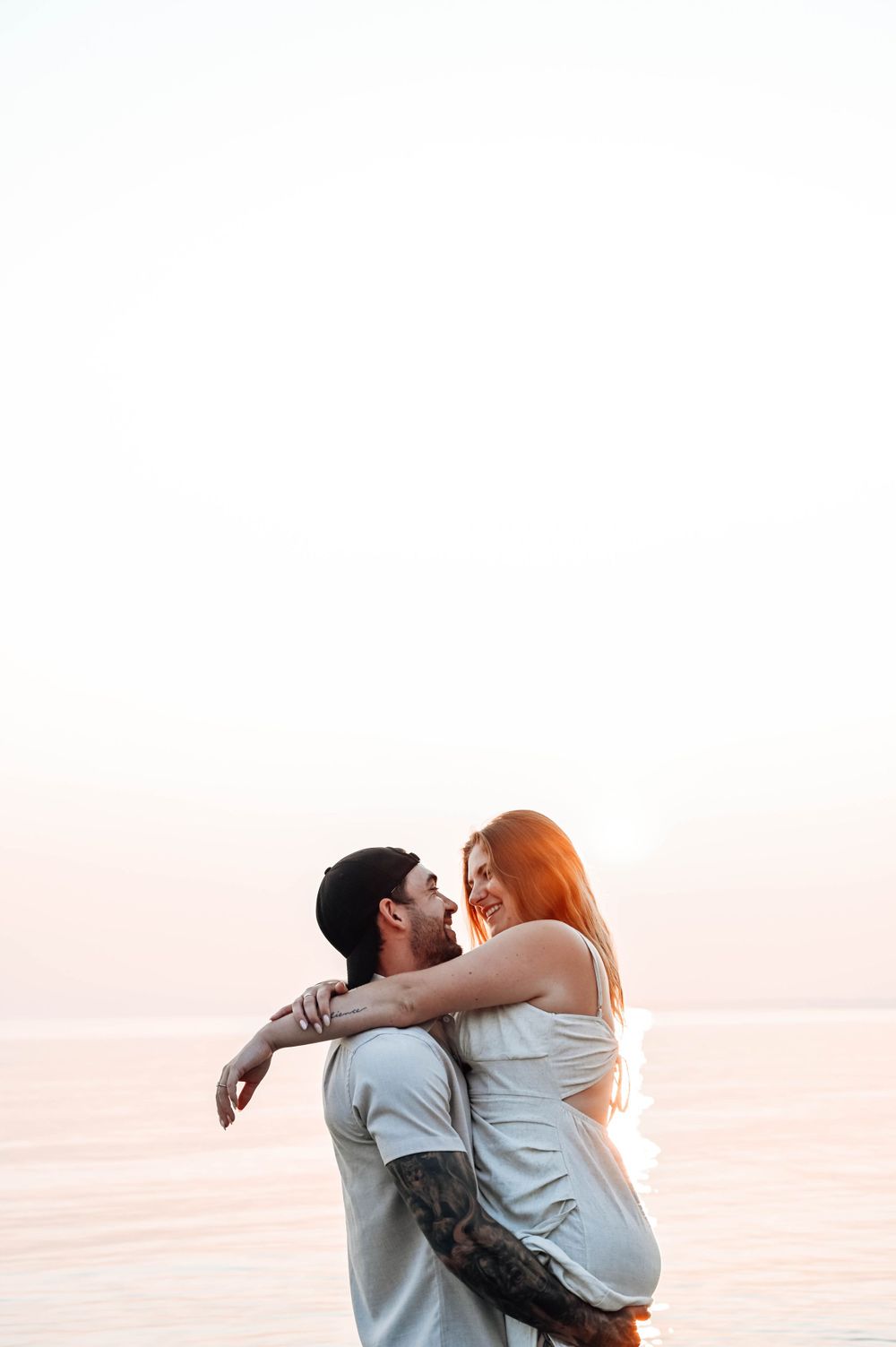 A tender moment between two people hugging near the water at sunset, bathed in warm golden light.