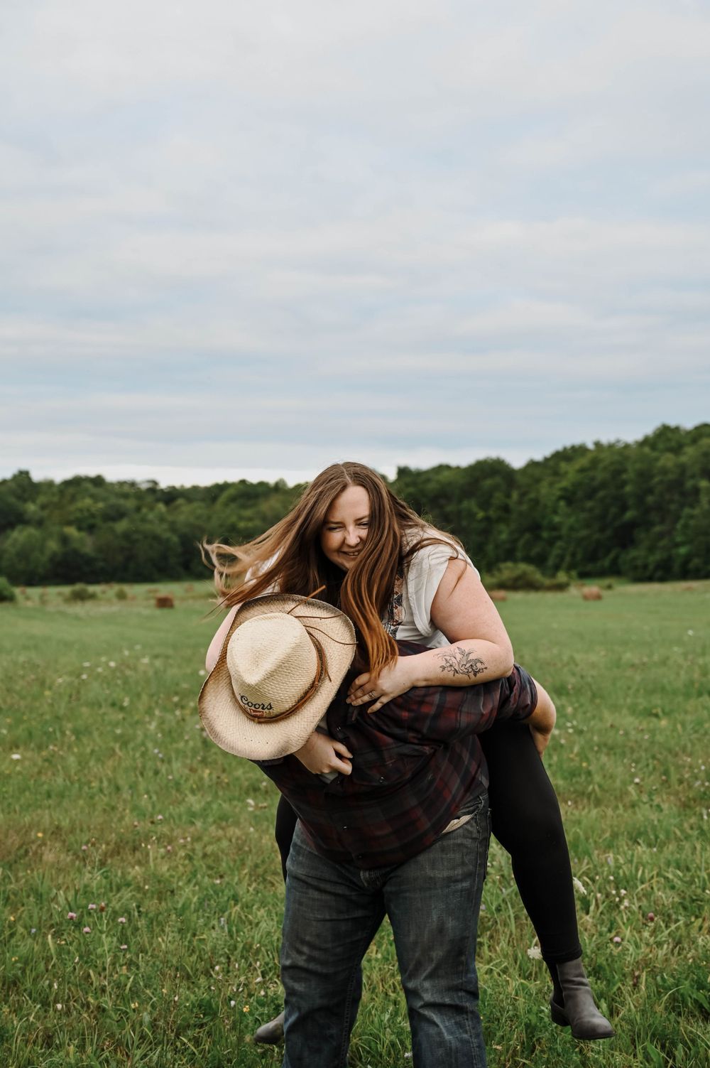 A playful couple shares a joyful moment in a green meadow on a cloudy day.