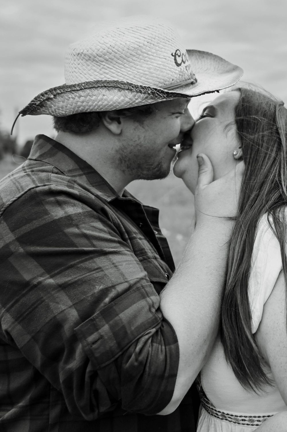A romantic black and white photograph of a couple sharing an intimate moment outdoors, with one wearing a cowboy hat.