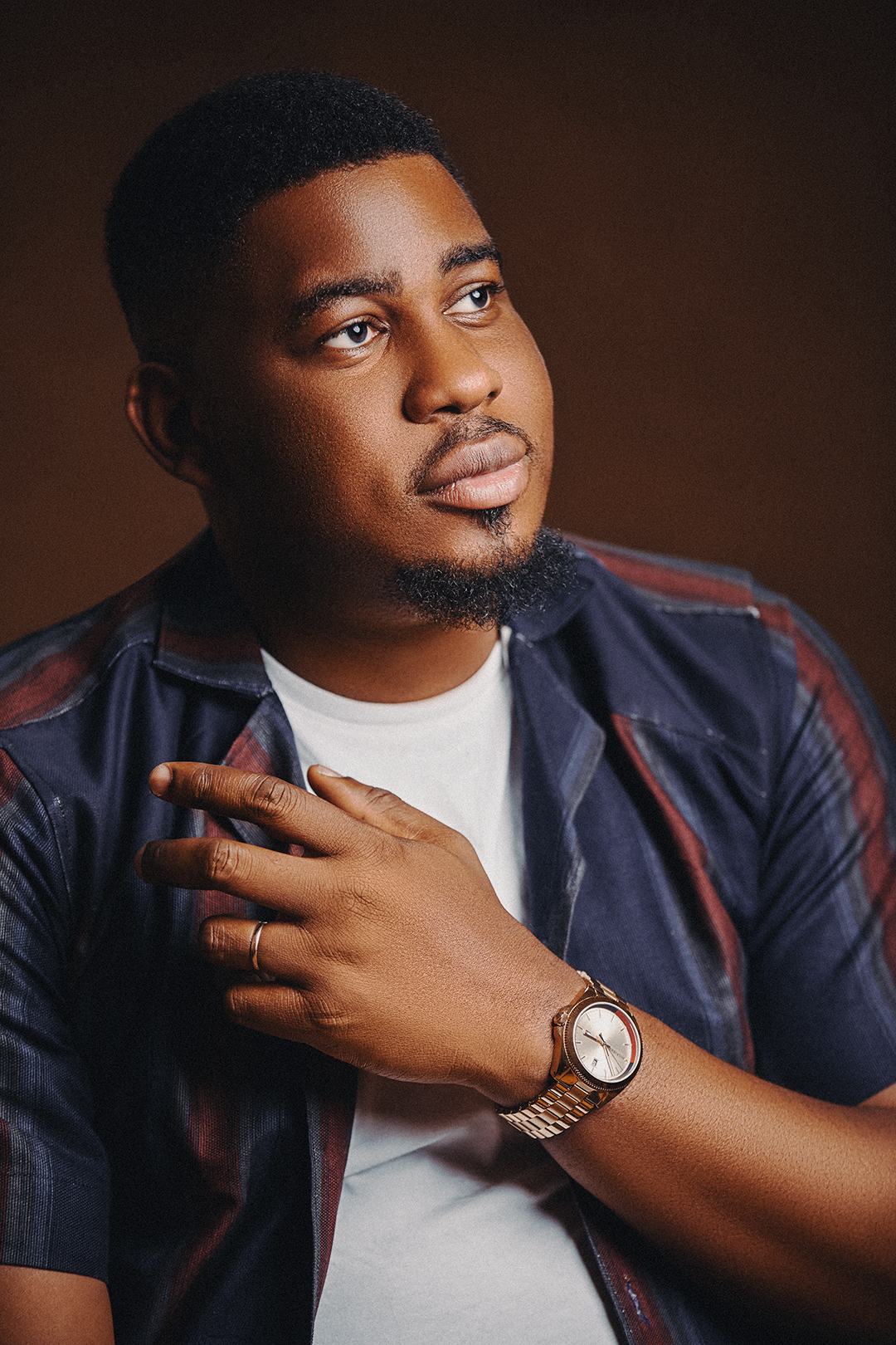 A portrait in a navy jacket wearing a gold watch against a brown background.