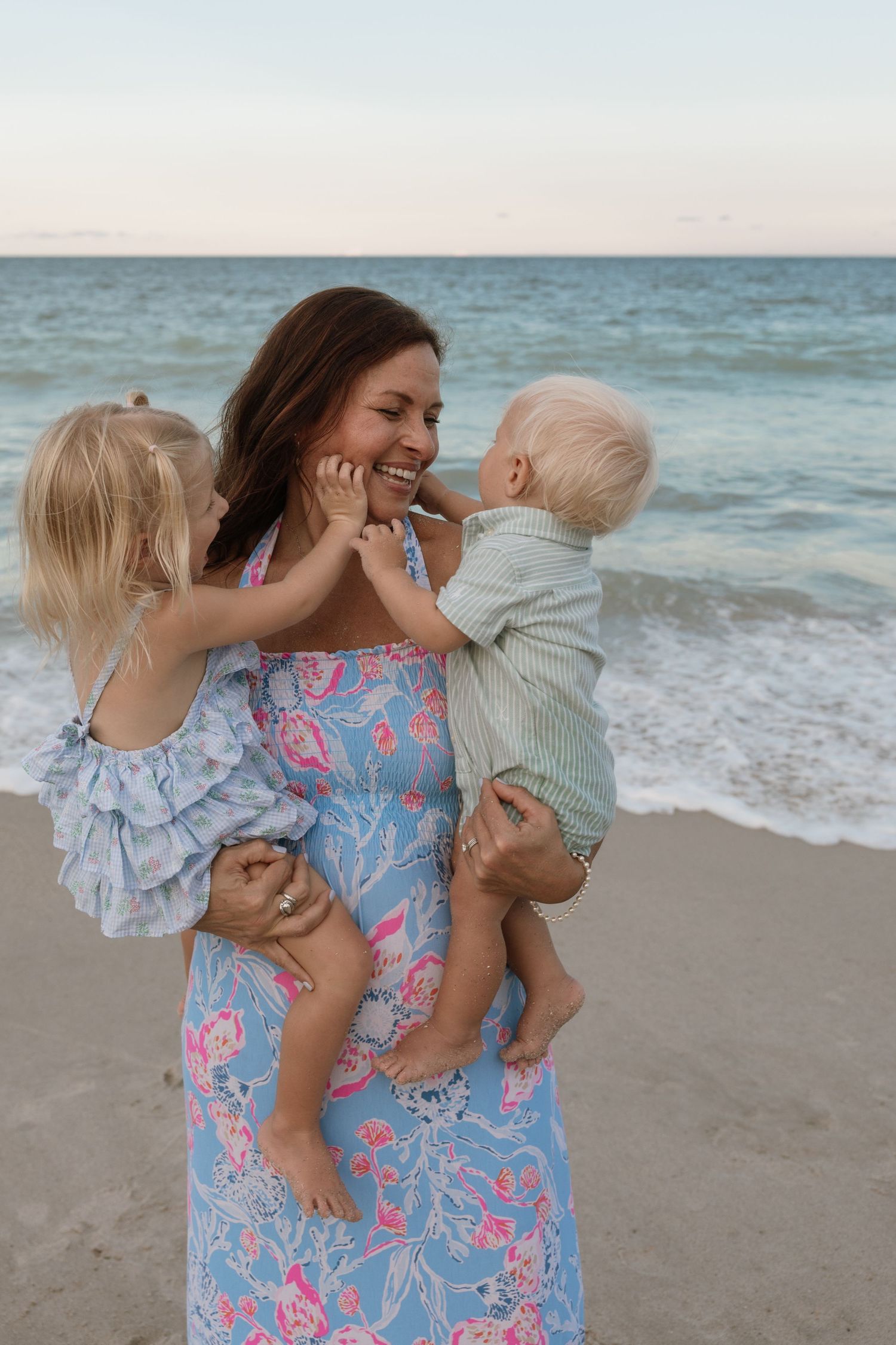 Family enjoying a playful moment together on a sunny beach with ocean waves in the background.