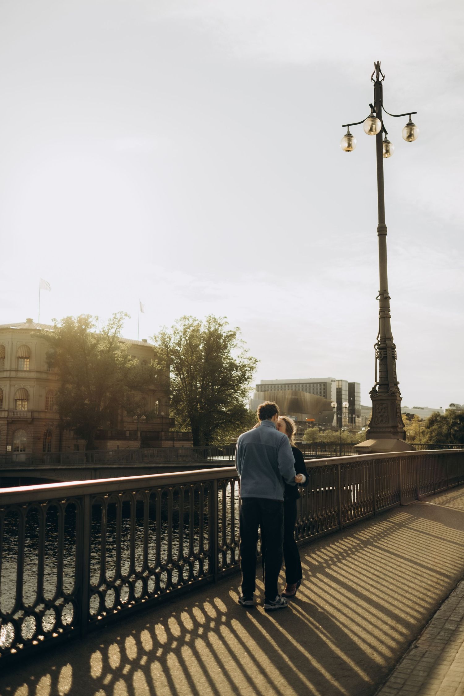 couple kissing on a bridge in afternoon sun during secret proposal photoshoot in Stockholm