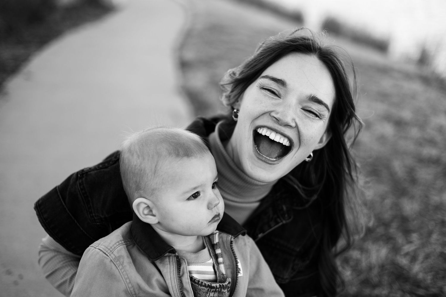 Black and white photo of a laughing young woman holding a cute baby outdoors on a path | Family photographer in  Westminster CO