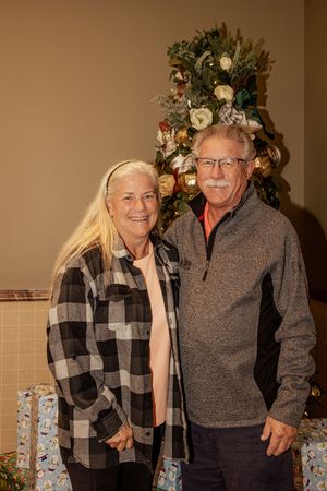 Two people share a lighthearted moment while posing for holiday photos in front of a Christmas tree.