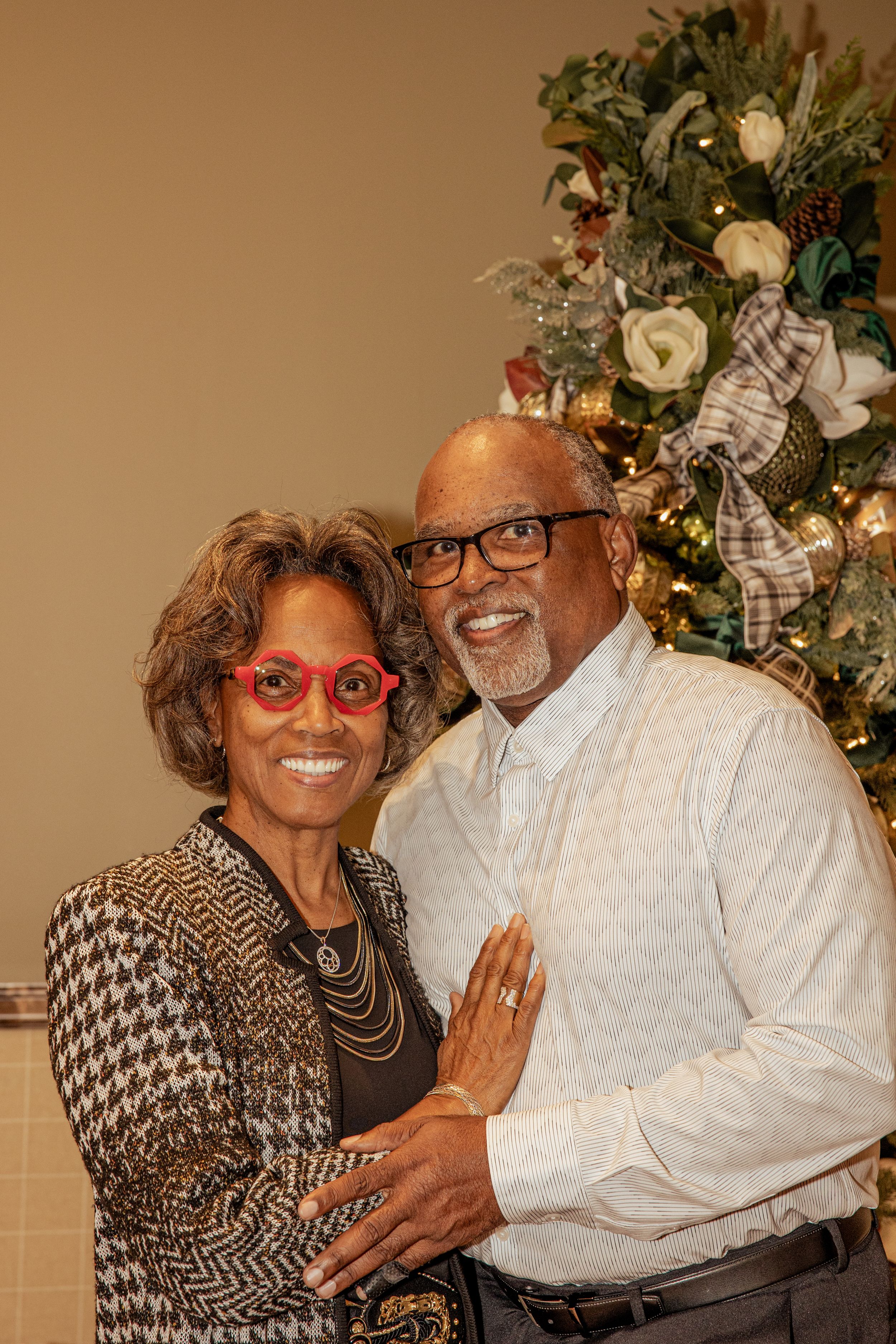 A couple in formal attire poses together in front of holiday decorations at a festive celebration.