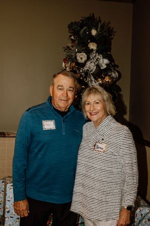Two guests pose together in front of a decorated Christmas tree at a holiday gathering.
