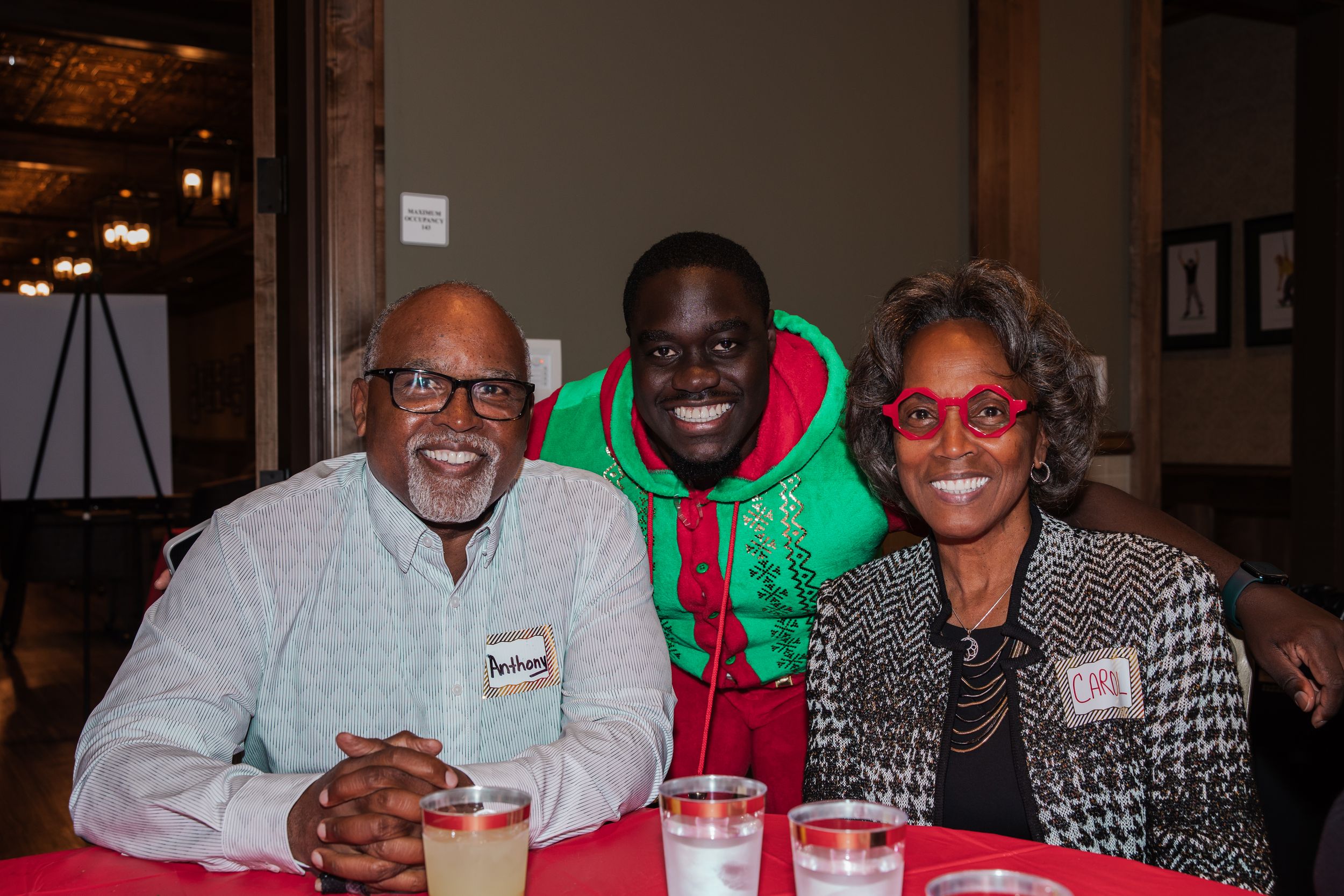 Three people smile together at a table during a holiday celebration.
