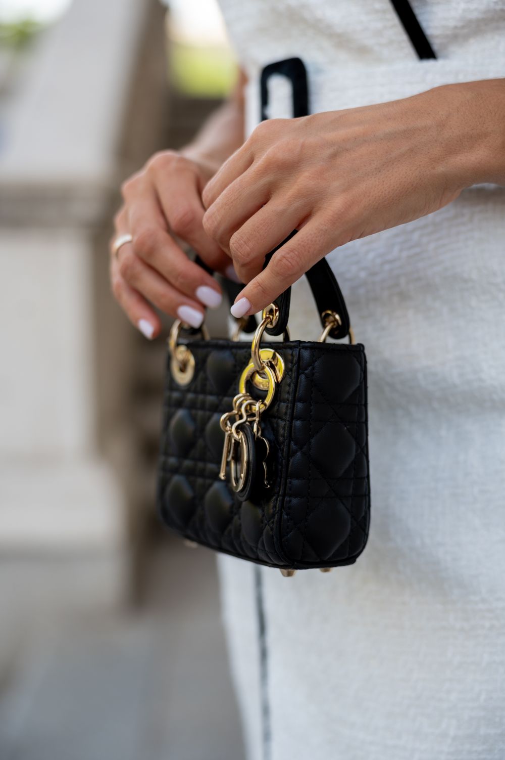 A series of images showing a black quilted handbag with gold hardware being held against a light gray background.