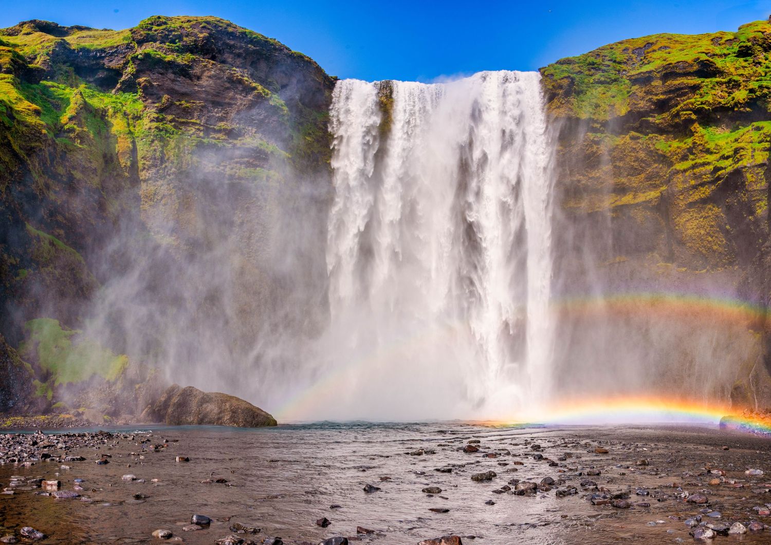 Majestic Skogafoss waterfall in Iceland creates a rainbow in its mist as it crashes onto the rocky shore.