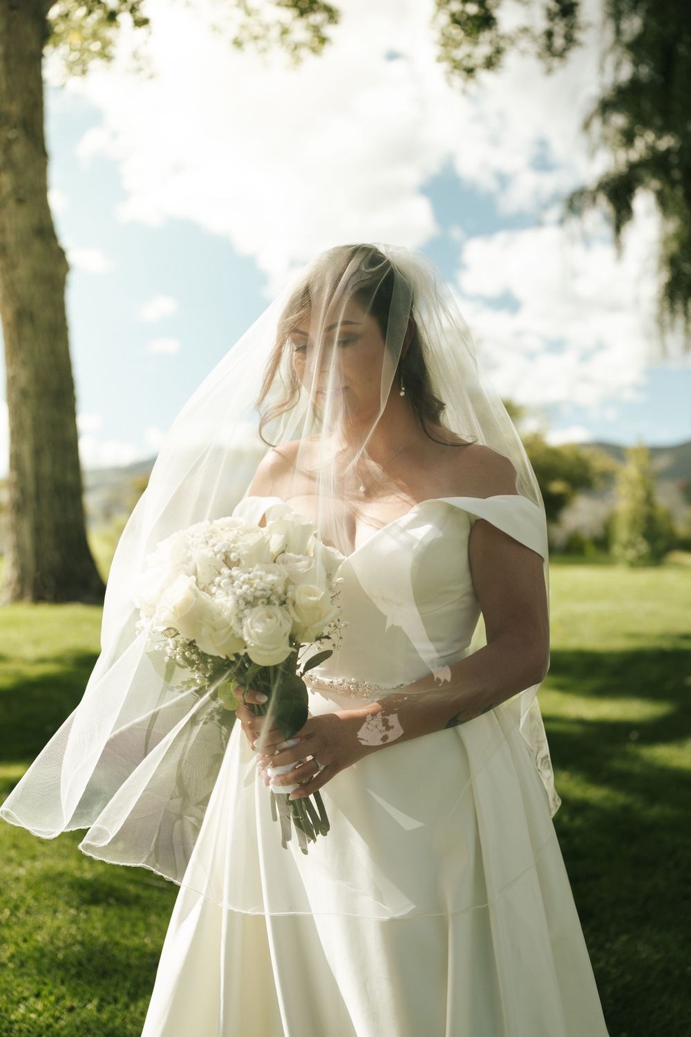 Bride holds a white bouquet while posing in an elegant wedding dress outdoors.