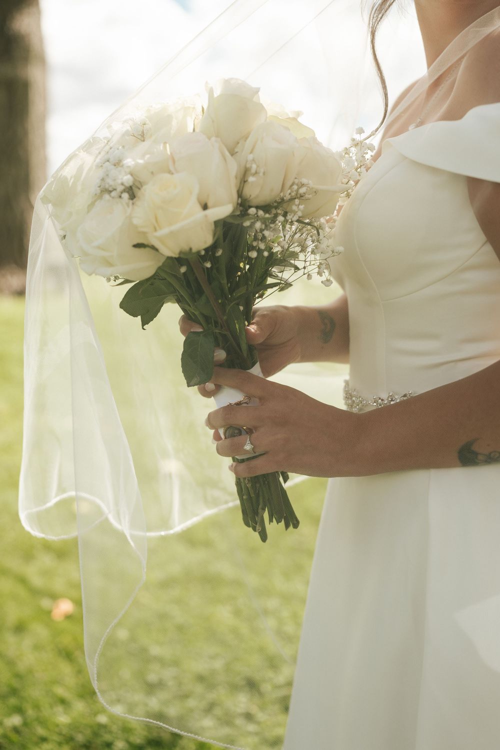 Close-up of white wedding bouquets with roses and baby's breath against flowing white dresses.