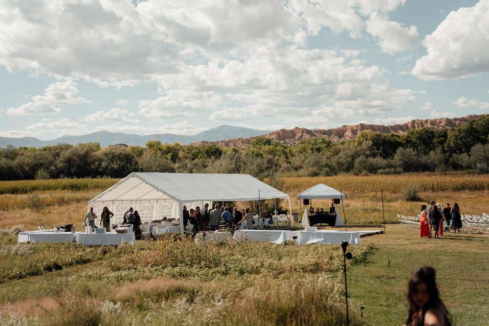 A panoramic view of a rural campsite with tents and small aircraft parked on grassy terrain under cloudy skies.