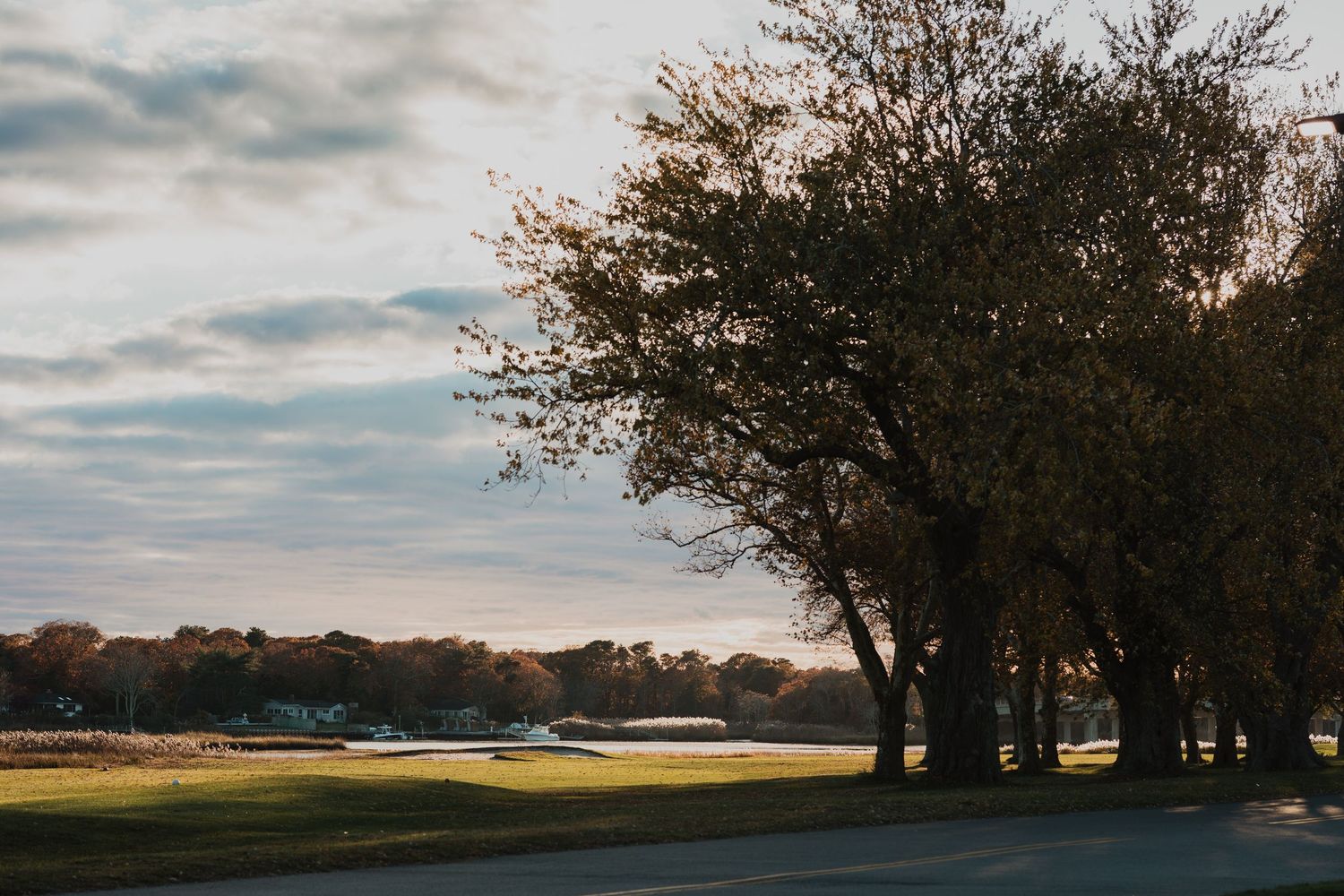 A scenic golf course at sunset with silhouetted trees lining the fairway and a cloudy sky overhead.