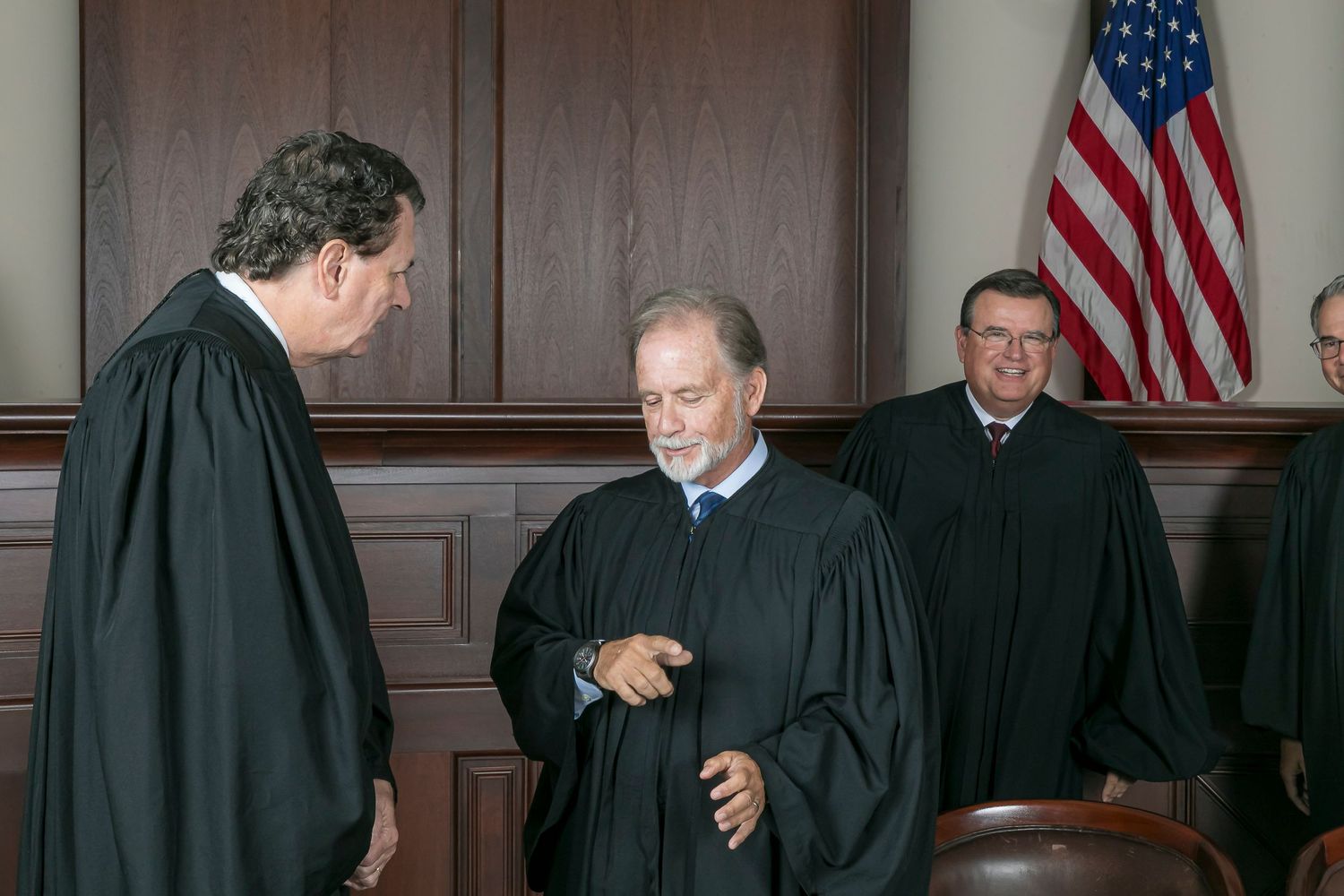 A judge wearing a black robe poses for a series of professional headshots against a backdrop with American flags.