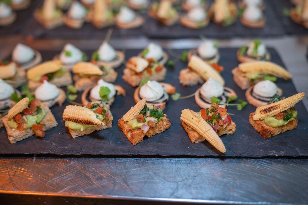 Elegant appetizers with creamy toppings and fresh herbs arranged on dark slate boards at a catered event.