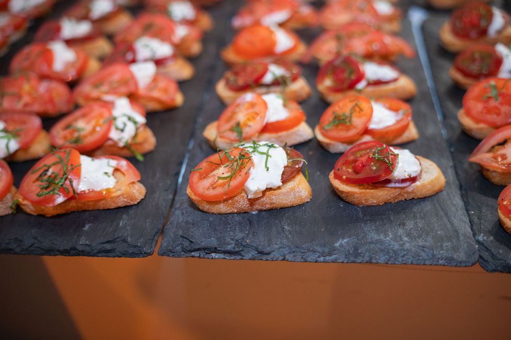 Rows of bruschetta topped with prosciutto and cream sauce displayed on dark serving platters.