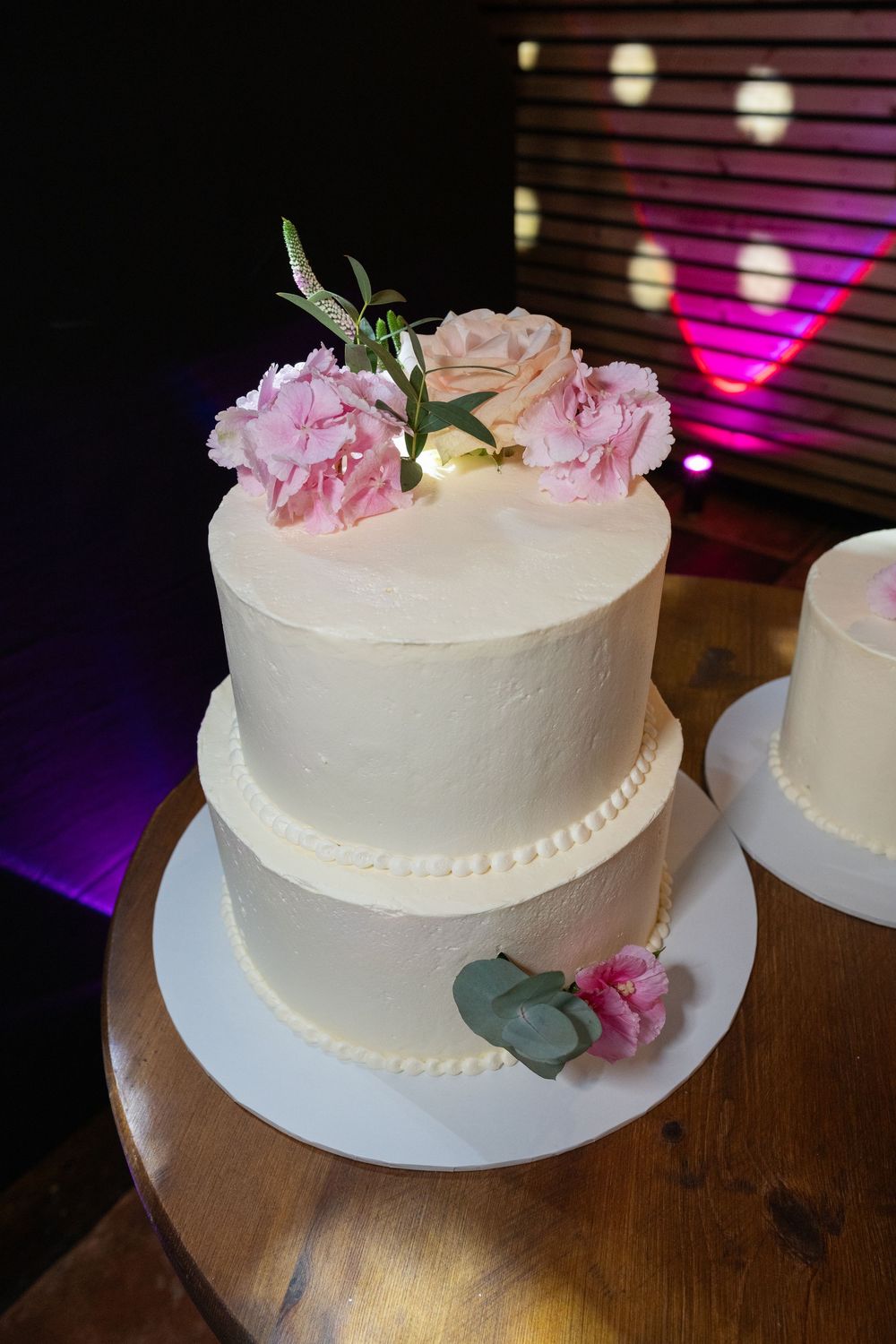 White wedding cake decorated with delicate pink roses and greenery on a wooden table.
