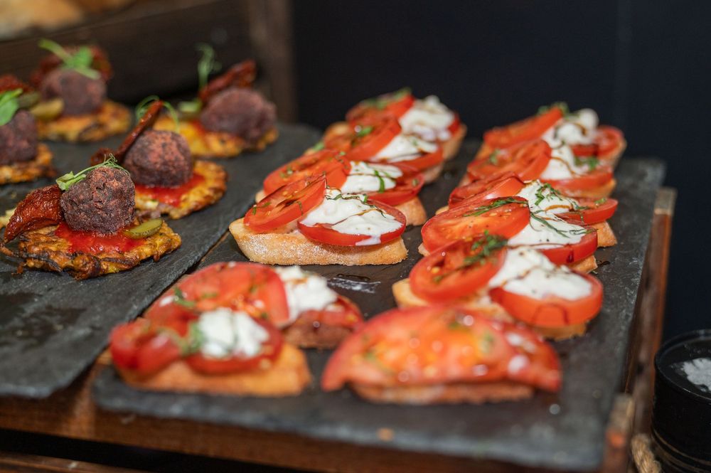 Artisanal bruschetta topped with fresh tomatoes and white cream sauce on slate platters.