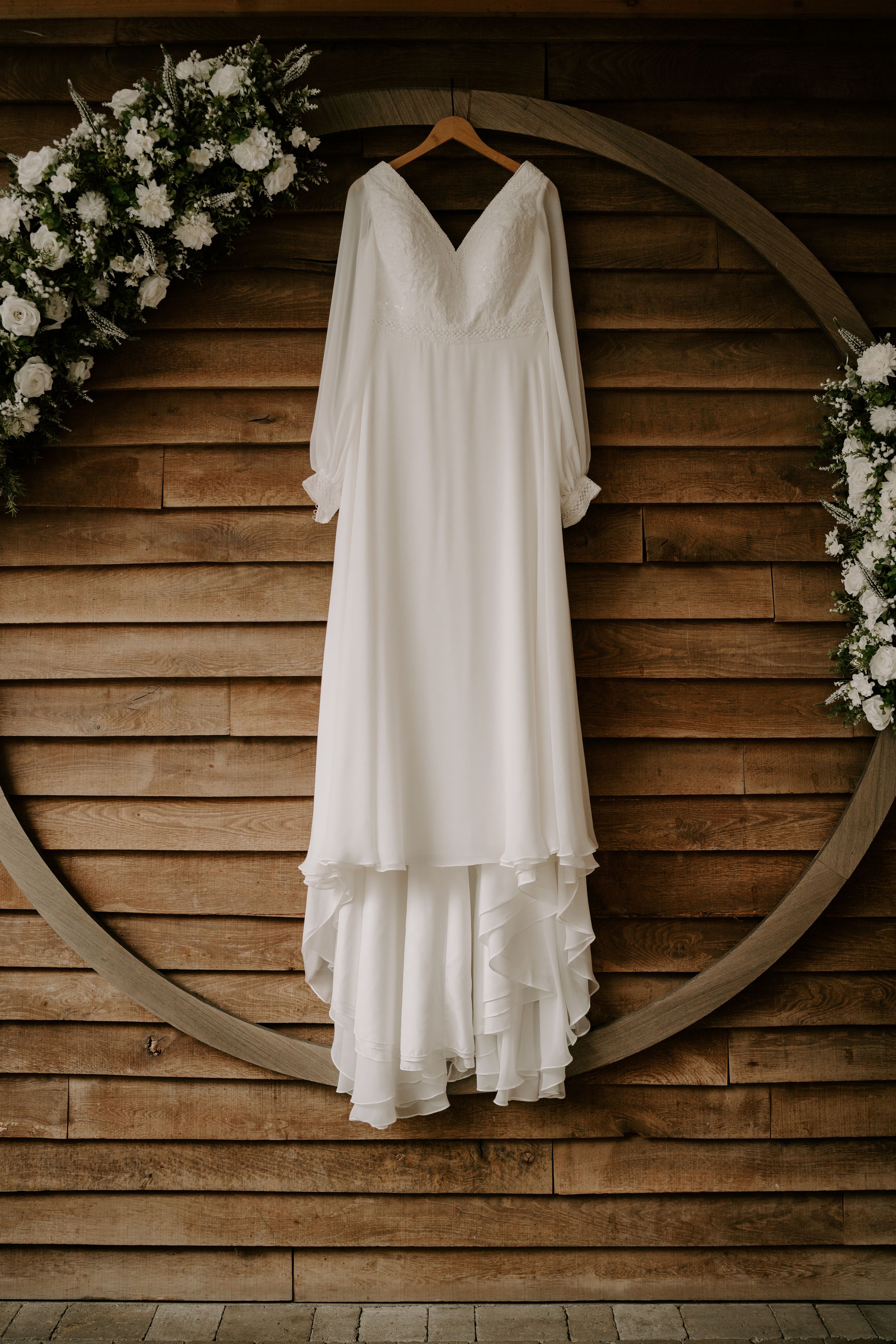 White wedding dress hanging on wooden wall with floral decorations.