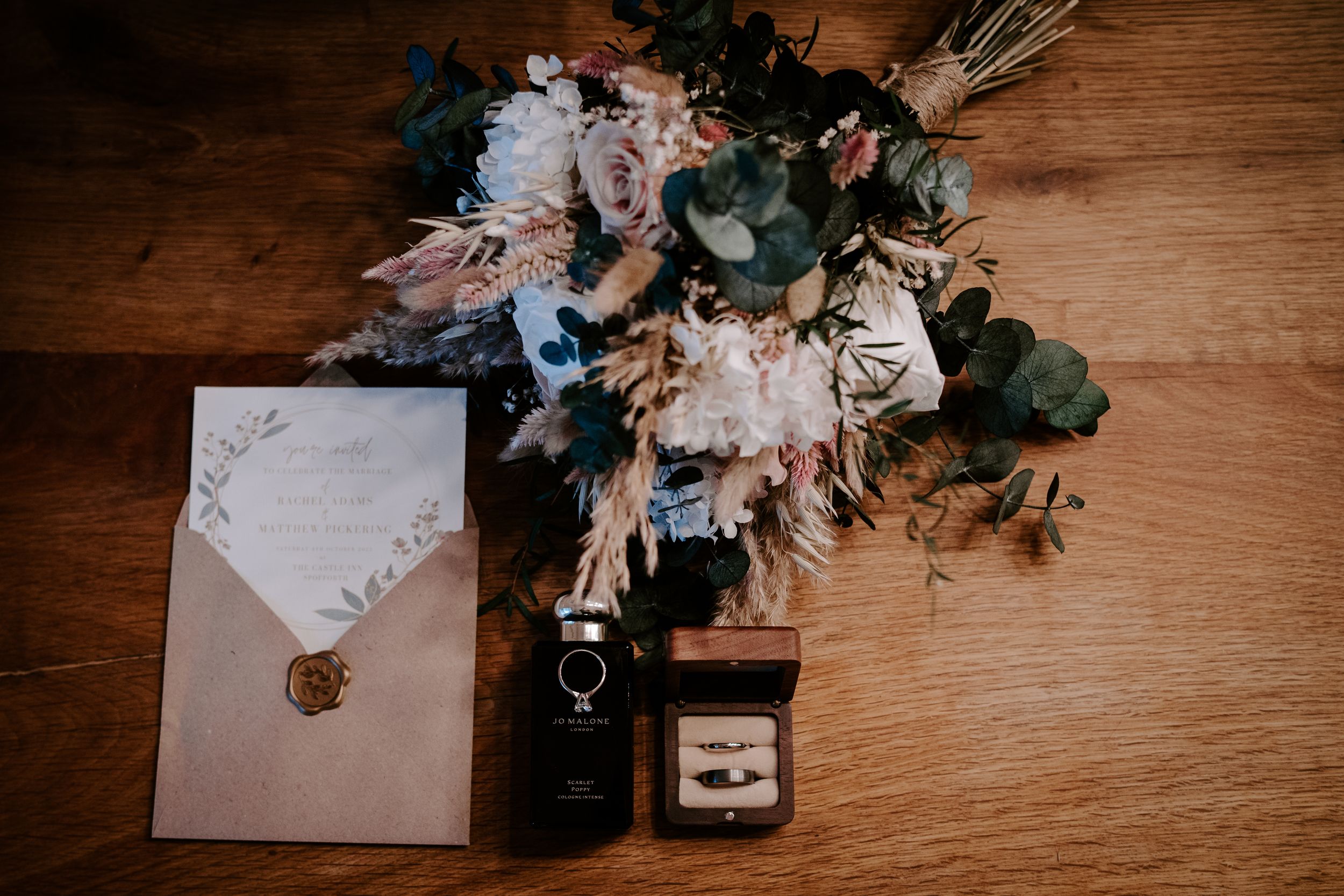 Wedding details arranged on rustic wooden surface with flowers, envelopes, and rings in vintage styling.