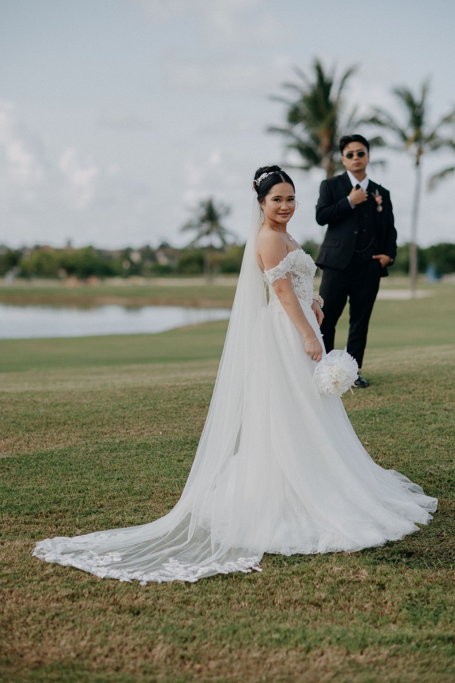 Wedding couple poses on grassy field with palm trees in the background.