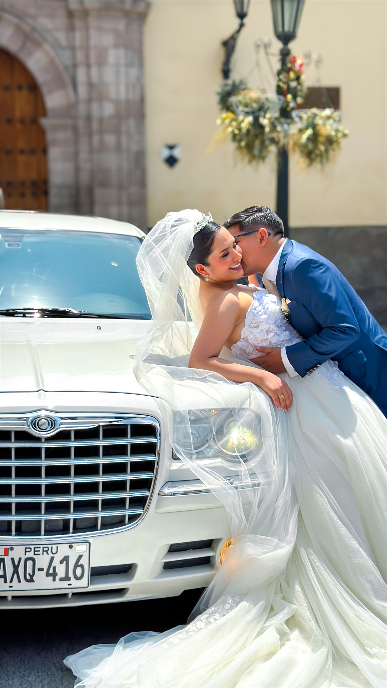 Elegant white wedding dress flowing beside luxury car with vintage lamp post in background.