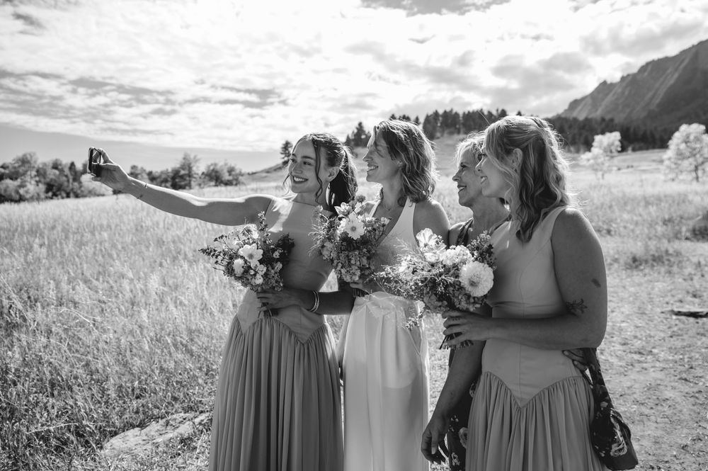 A group of bridesmaids in flowing dresses hold bouquets while standing together in a scenic mountain landscape.