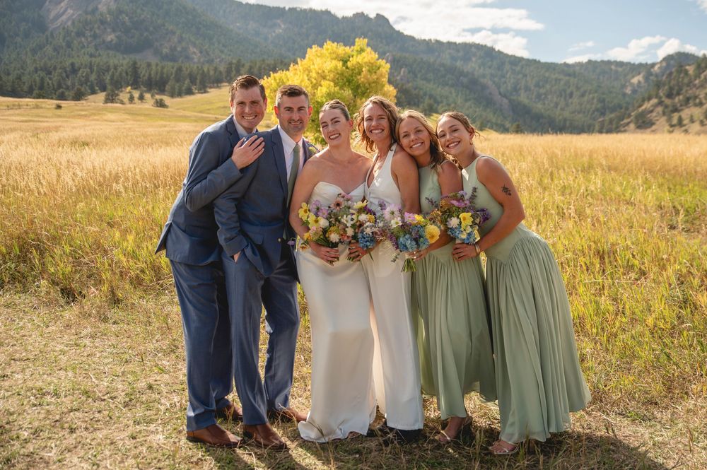 A group poses together in a scenic mountain meadow with golden grass and evergreen trees in the background.