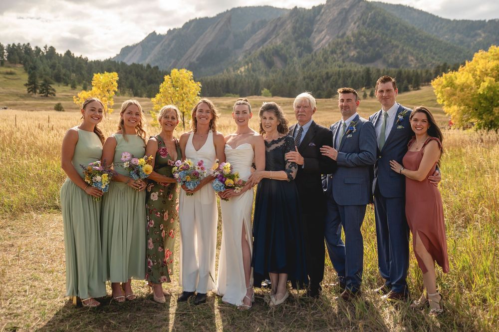 Wedding party poses together in front of scenic mountain landscape with golden autumn grass and evergreen trees.