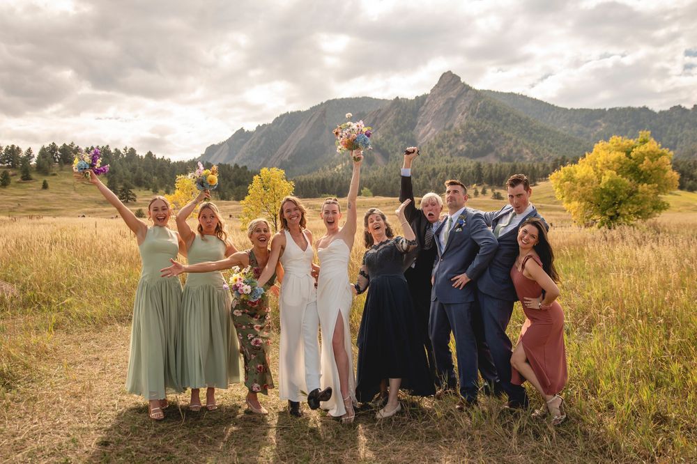 Wedding party poses together in scenic mountain meadow during golden hour with dramatic cloudy sky.