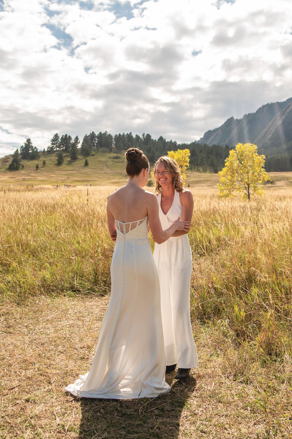 A romantic golden hour photoshoot in a mountain meadow with tall grass and autumn trees in the background.
